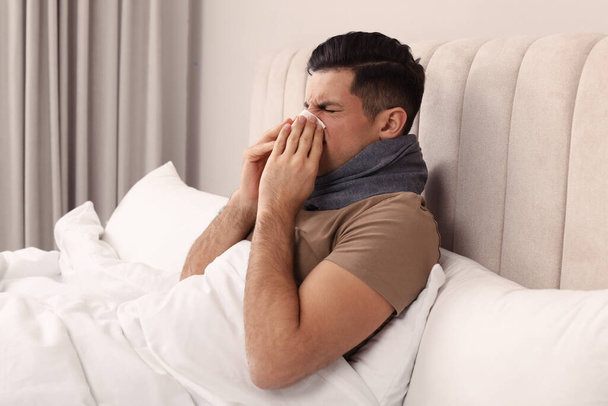 Sick man with scarf and tissue suffering from cold in bed at home - Fotografie, Obrázek