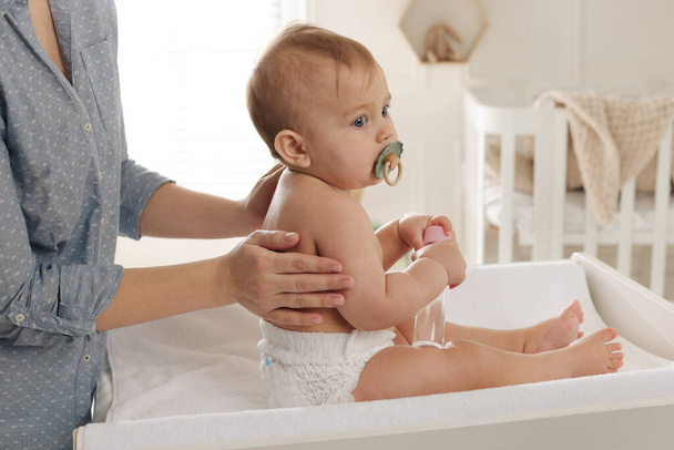 Mother massaging her cute baby with oil on changing table at home, closeup - Photo, Image