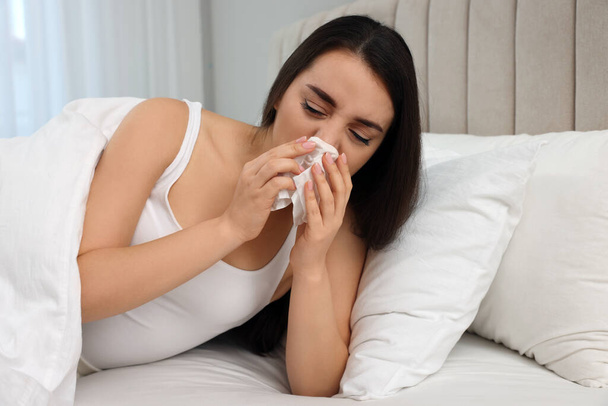 Sick young woman with tissue in bed at home - Foto, afbeelding