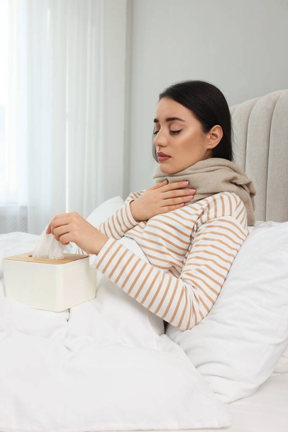Sick young woman with box of tissues in bed at home - Fotó, kép