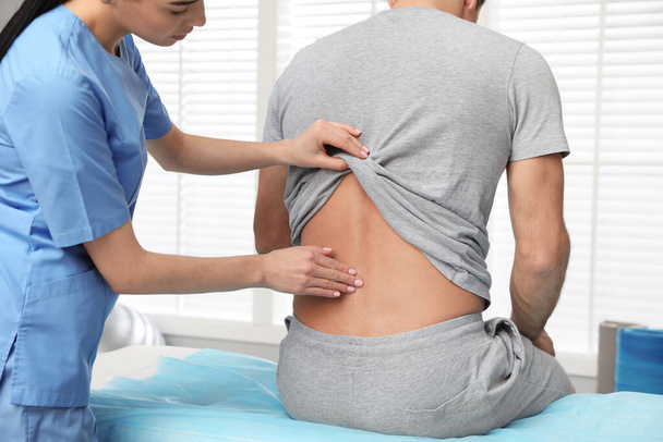 Orthopedist examining man's back in clinic. Scoliosis treatment - Фото, изображение