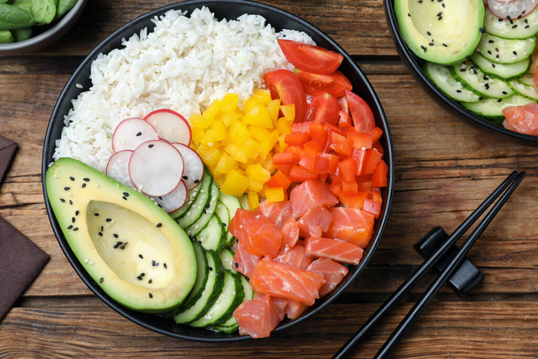 Delicious poke bowl with salmon and vegetables served on wooden table, flat lay - Фото, зображення