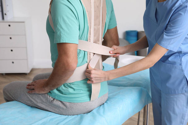 Orthopedist helping patient to put on posture corrector in clinic, closeup. Scoliosis treatment - Φωτογραφία, εικόνα