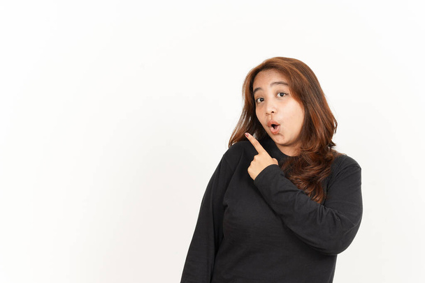 Pointing Produkt auf der Seite der schönen asiatischen Frau trägt schwarzes Hemd isoliert auf Weiß - Foto, Bild