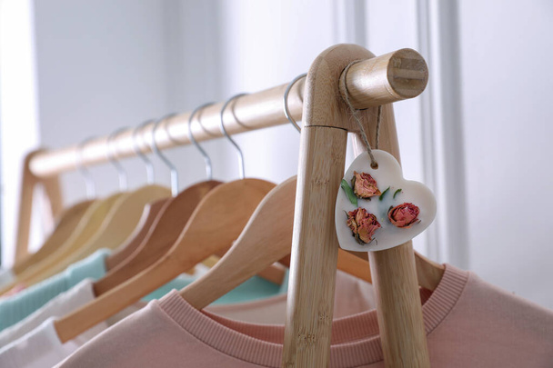 Beautiful heart shaped scented wax sachet and clothes hanging on wooden rack indoors, closeup - Photo, Image