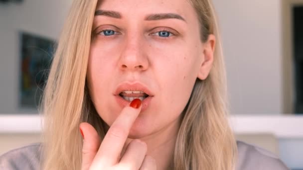 Portrait of a young girl applying a moisturizing balm to her lips. Beautiful blue-eyed blonde cares for her face, looking into the camera, slow motion, 4k - Footage, Video