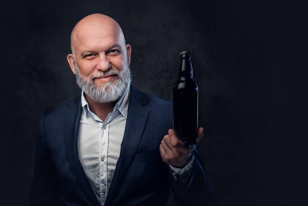 Cool starší muž drží láhev proti tmavému pozadí - Fotografie, Obrázek
