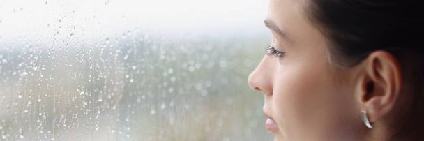 Junge nachdenkliche Frau blickt bei Regen aus dem Fenster - Foto, Bild