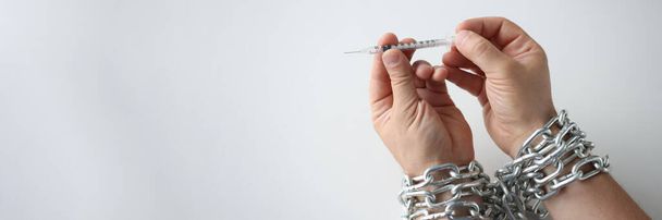 Man with hands tied with metal chain holding syringe with drugs closeup - Photo, Image