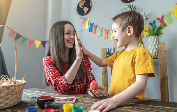 Mom and little son together are coloring eggs, having fun and giving five to each other. Concept of family preparation for Easter, festive spring mood. - Foto, Imagem