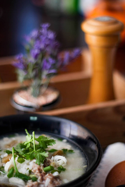 Varkensgekookte rijst met shiitake champignons op een zwarte kom met een lepel op tafel is het ontbijt van Aziaten. - Foto, afbeelding