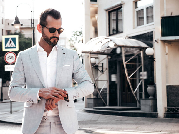 Portrait of handsome confident stylish hipster lambersexual model.Sexy modern man dressed in elegant white suit. Fashion male posing in the street background in Europe city at sunset. In sunglasses - Foto, afbeelding
