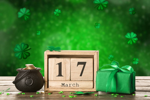 Maceta con monedas, calendario y caja de regalo en la mesa sobre fondo verde. Celebración del Día de San Patricio - Foto, Imagen
