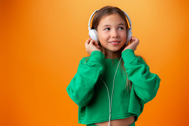 Portrait of modern happy teen school girl with headphones on orange background - Foto, imagen