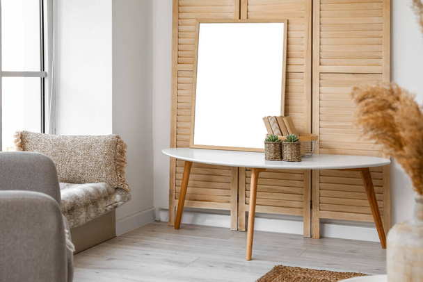 Кавовий столик з рамкою, книжками та вазонами біля дерев'яного розкладного екрану у вітальні
 - Фото, зображення