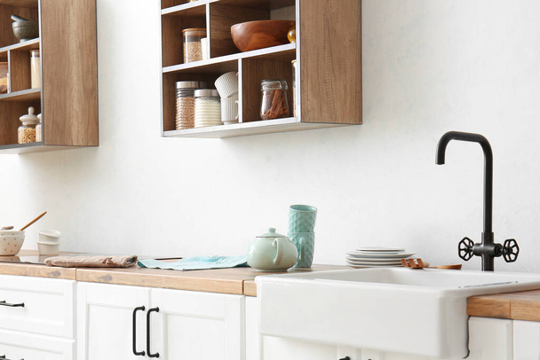 Teekanne mit Tassen auf dem Tresen in der Nähe der Lichtwand in der Küche - Foto, Bild