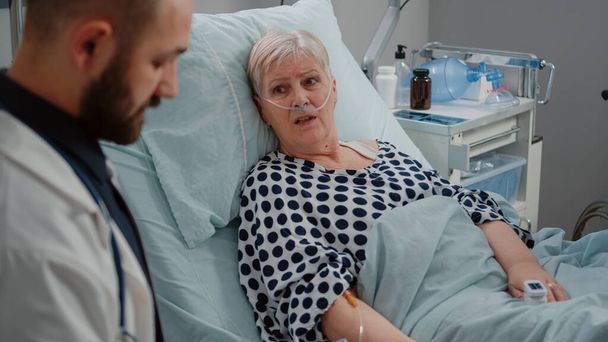 Κοντινό πλάνο του ηλικιωμένου ασθενή που βρίσκεται στο κρεβάτι και μιλάει με το γιατρό - Φωτογραφία, εικόνα