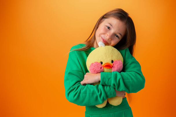Teenage girl embracing toy duck against orange background - 写真・画像