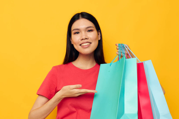 Portrait Asian beautiful young woman with multicolored shopping bags yellow background unaltered - Foto, imagen