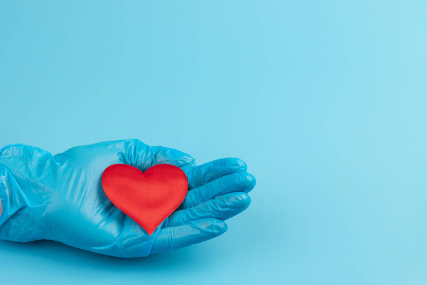 Mujer médico manos sosteniendo y cubriendo el corazón de juguete rojo primer plano. Concepto de cardiología. - Foto, imagen