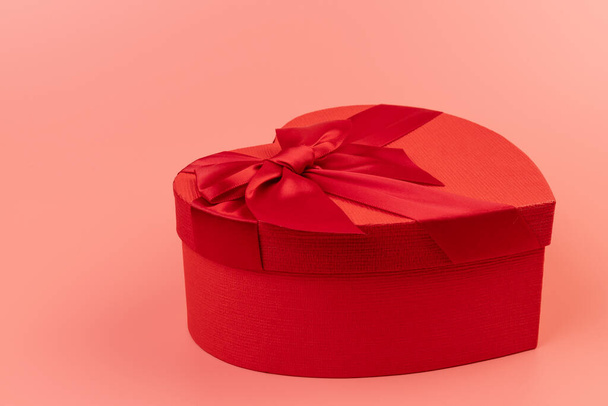Red heart-shaped gift box with a red ribbon on pink background. Happy Valentine's Day. Anniversary.  - Valokuva, kuva