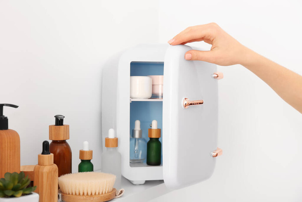 Mano femenina con refrigerador pequeño y productos cosméticos en el estante - Foto, imagen