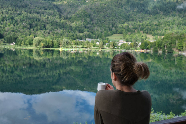 unrecognizable woman drinking coffee in front of the lake of her rural accommodation - Photo, Image
