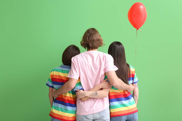 Man and two beautiful women in rainbow clothes and with balloon on color background, back view. Concept of polyamory and LGBT - Photo, Image