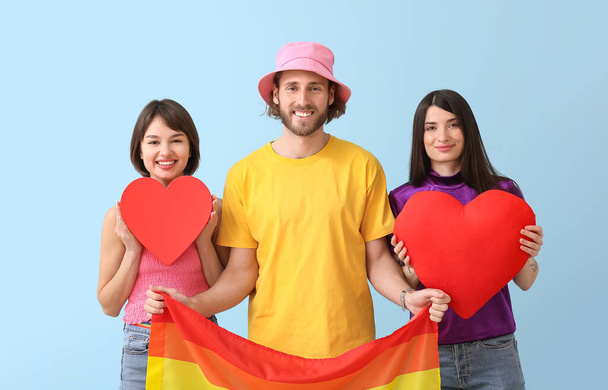 Man and two beautiful women with rainbow flag and red hearts on color background. Concept of polyamory and LGBT - Photo, Image