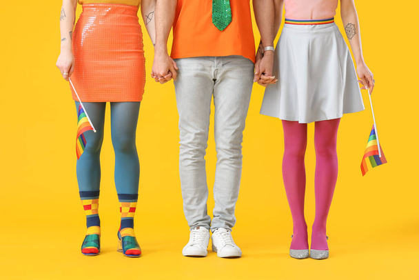 Hombre y dos mujeres hermosas en ropa colorida y con banderas de arco iris en el fondo de color. Concepto de poliamory y LGBT - Foto, imagen