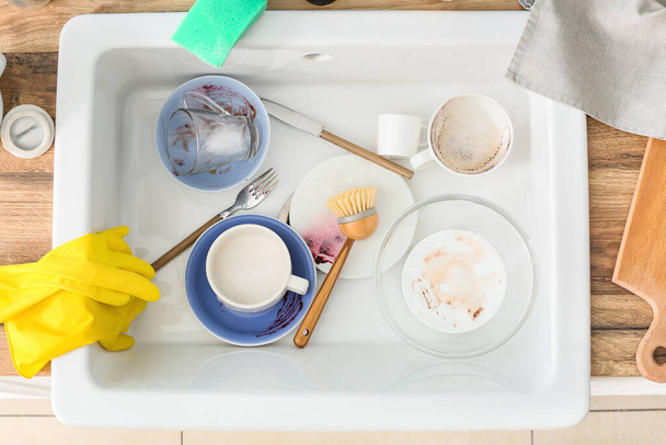 Грязная посуда и чистящая щетка в керамической раковине - Фото, изображение