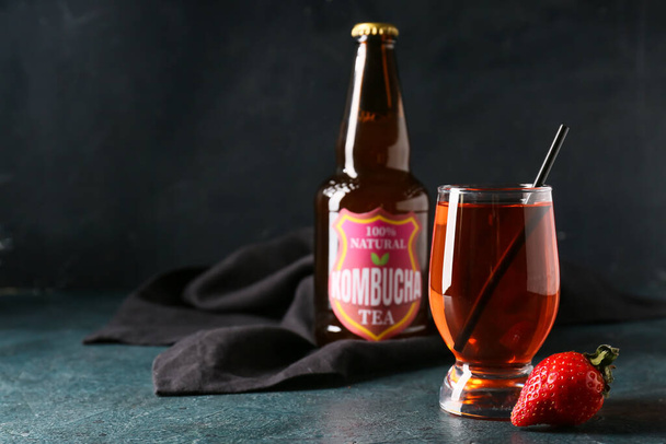 Flasche und Glas frischer Erdbeer-Kombucha auf dunklem Hintergrund - Foto, Bild