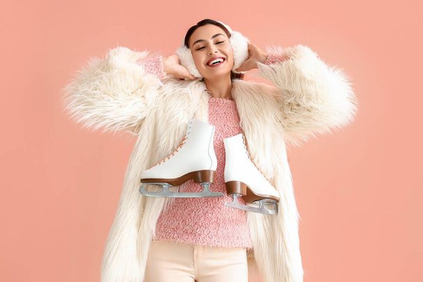 Mujer joven feliz en ropa de abrigo con patines de hielo sobre fondo rosa - Foto, Imagen