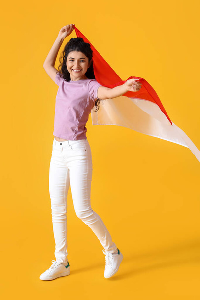 Onnellinen aasialainen nainen Indonesian lipun kanssa keltaisella taustalla - Valokuva, kuva