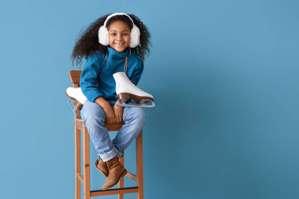 Little African-American girl with ice skates sitting in chair on blue background - Zdjęcie, obraz
