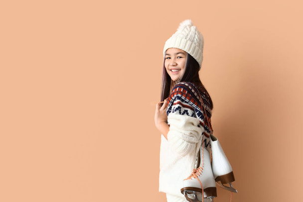 Little Asian girl in warm clothes with ice skates on beige background - Photo, Image