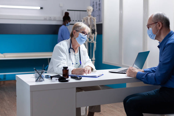 Specialist with face mask signing checkup papers at medical consultation with man - Photo, Image