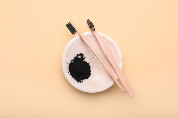Plate with activated charcoal tooth powder and toothbrushes on beige background - Fotó, kép