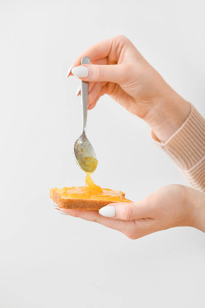 Woman spreading tasty orange jam onto toast on light background - Foto, Imagem