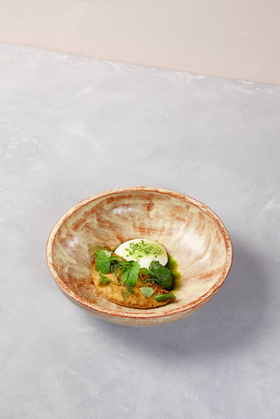 Omelette with creamy espuma, spinach sorbe and green leaves. Omelette in homemade ceramic bowl on gray stone background. Ceramic still life. Breakfast in modern serveware - Fotó, kép