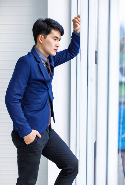 Millennial Asian handsome smart confident professional success male manager businessman entrepreneur in formal blue suit smiling standing near skyscraper office window - Valokuva, kuva