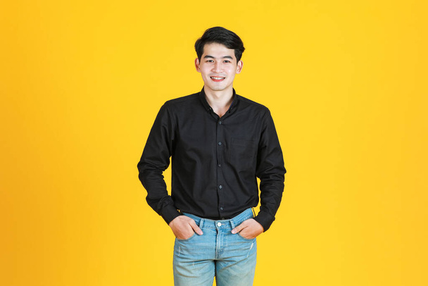 Portrait studio shot of Asian young man professional successful male businessman in casual black shirt standing smiling look at camera on yellow background - Photo, image
