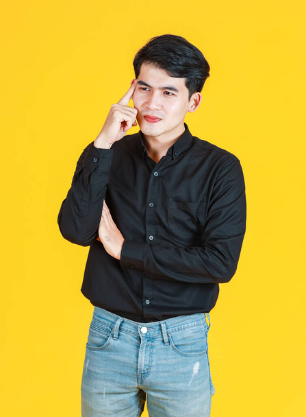 Milenyum Asyalı, düşünceli, başarılı, sıradan gömlekli ve kot pantolonlu iş adamının sarı arka planda parmağını gösteren bir portre resmi.. - Fotoğraf, Görsel