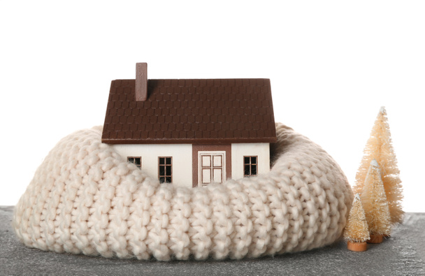 Σπίτι μοντέλο με ζεστό κασκόλ και διακοσμητικά έλατα στο τραπέζι σε λευκό φόντο. Έννοια θέρμανσης - Φωτογραφία, εικόνα
