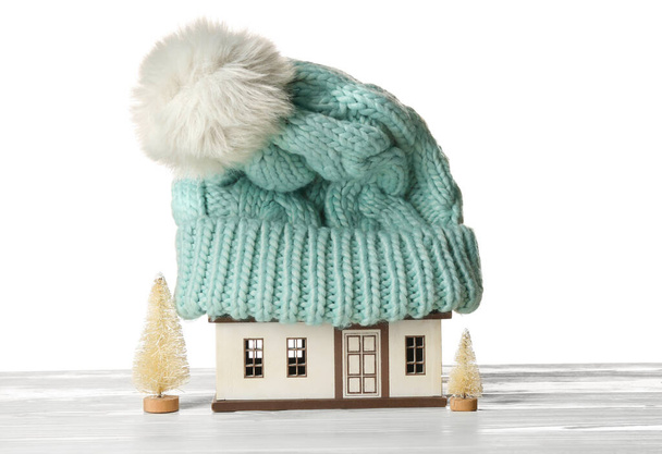 白い背景にテーブルの上の帽子と装飾的なモミの木と家のモデル。暖房コンセプト - 写真・画像