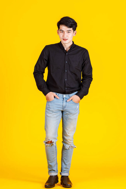 Портретная студия, снятая успешным бизнесменом азиатского происхождения в повседневной одежде с черным длинным рукавом, держащимся за руку и рвущим джинсовый карман на желтом фоне. - Фото, изображение