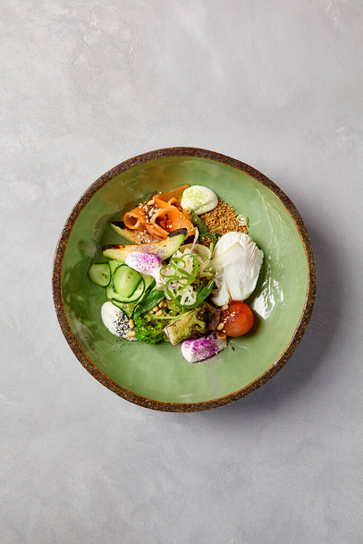 Salad bowl with salmon, avocado, broccoli, vegetables and egg on homemade ceramic plate. Buddha bowl with salmon, broccoli, quinoa in modern serveware. Modern ceramic dishware on concrete background - Photo, Image