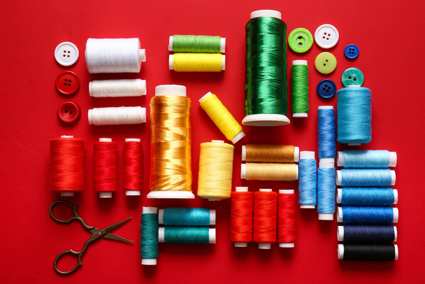 Bobines de fil avec boutons et ciseaux sur fond rouge - Photo, image