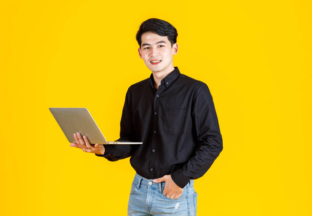 Porträt Nahaufnahme Studioaufnahme von asiatischen Mann glücklich männlichen Geschäftsmann Modell in lässigem Outfit stehend mit Laptop-Computer für Werbung auf gelbem Hintergrund - Foto, Bild