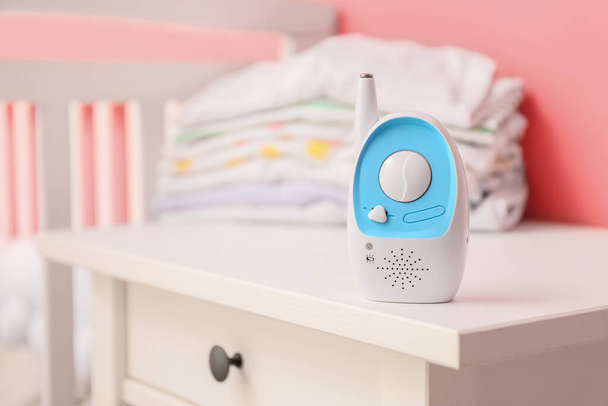 Modern baby monitor and stack of clothes on table near color wall - Fotoğraf, Görsel
